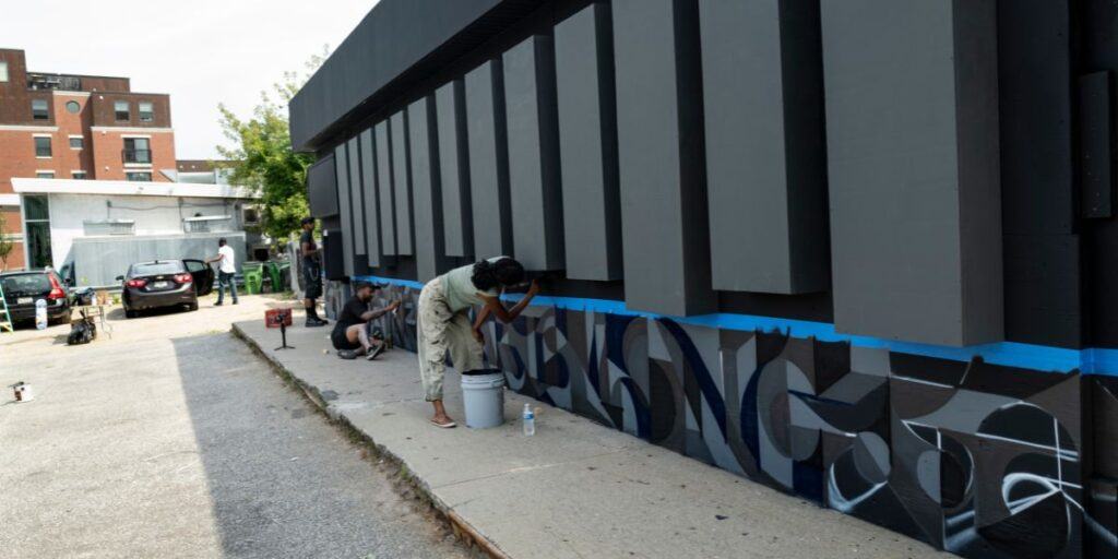 Artist paints a mural on a building wall, contributing to rich Portland Maine history.