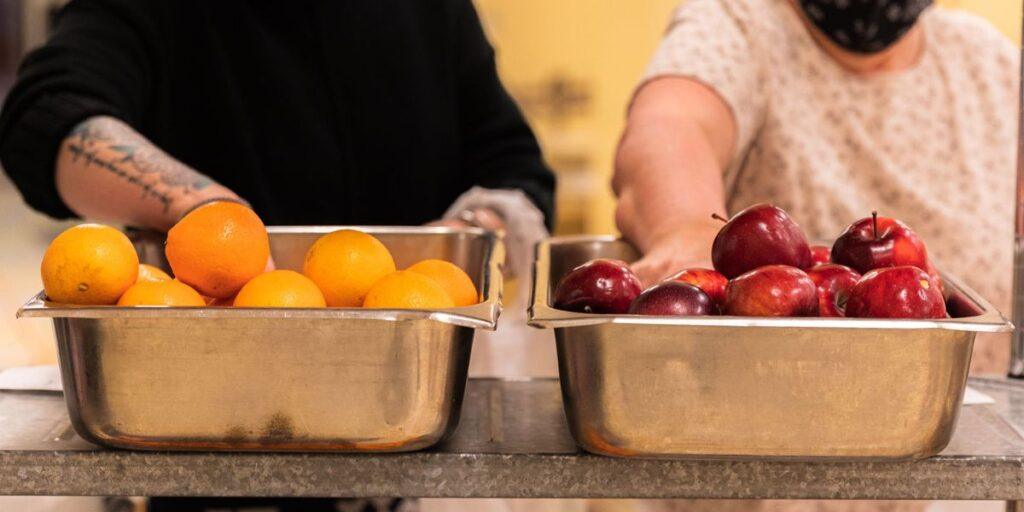 Two people serving fresh oranges and apples at Portland Maine luxury hotel buffet.