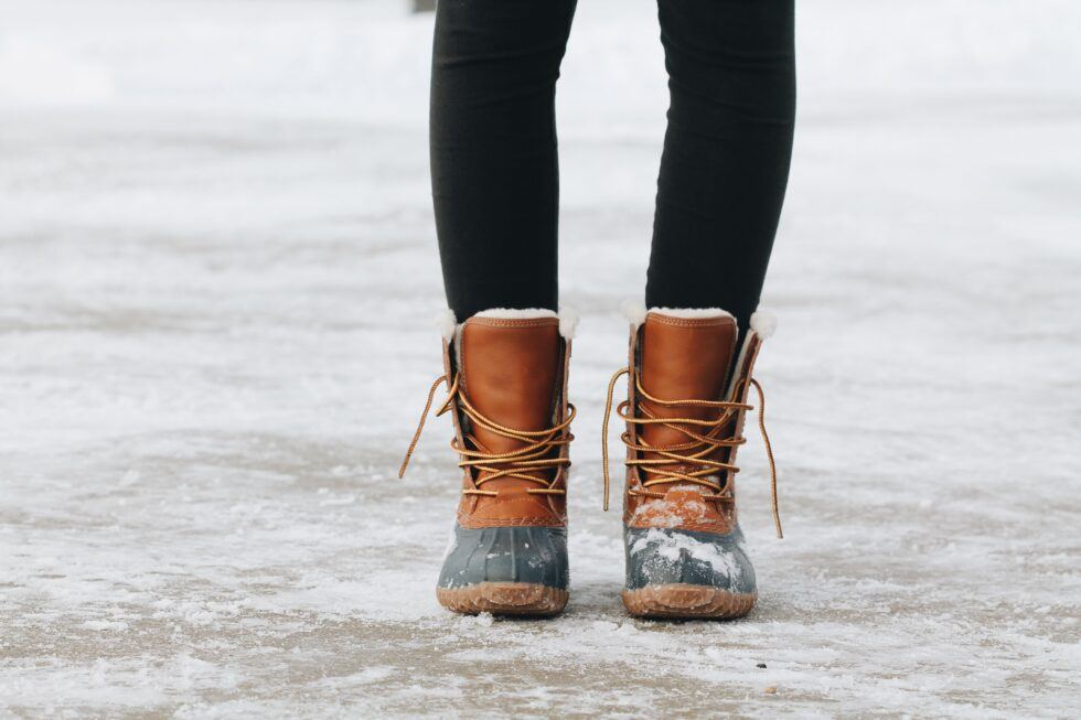 Person wearing brown snow boots standing on icy ground. Explore places to stay in Portland Maine.